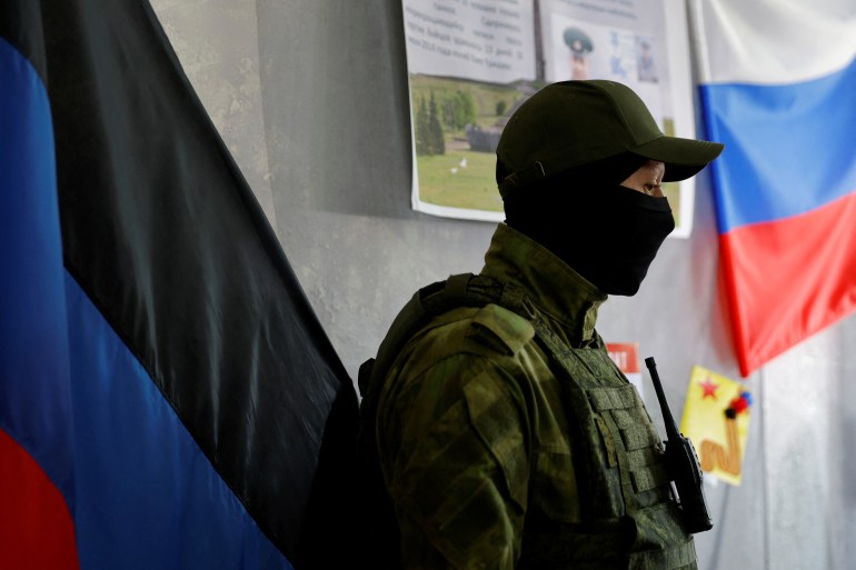 A member of the self-proclaimed Donetsk People's Republic stands guard at a polling station with a Russian flag on the wall ahead of Friday's referendum.