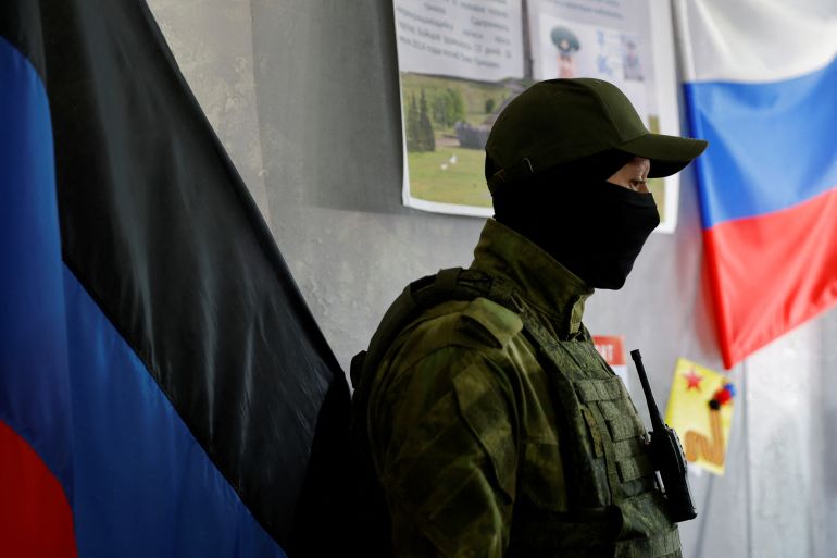 A member of the self-proclaimed Donetsk People's Republic stands guard at a polling station with a Russian flag on the wall ahead of Friday's referendum.