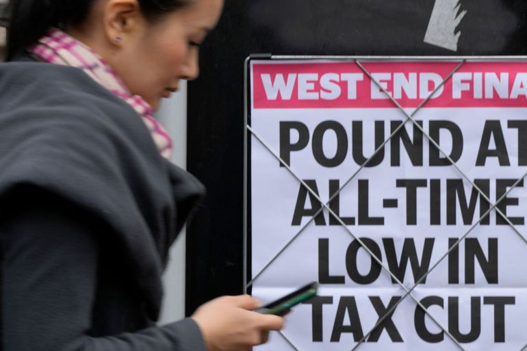 A woman walks past a headline posted on a wall announcing the Pound at an all time low