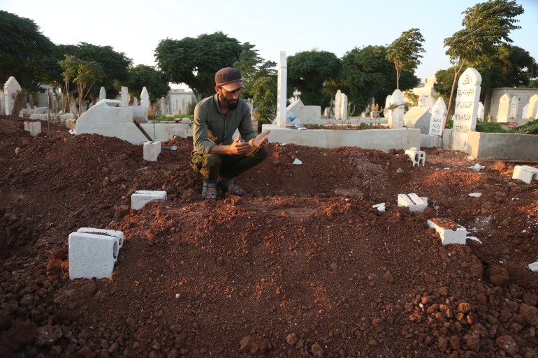 A man prays at a freshly dug grave in a Syrian cemetry