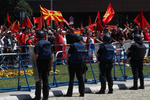 People wave the old and the current national flags and chant slogans during a protest, while police officers guard the entrance of the parliament building in Skopje, North Macedonia, on Saturday, July 16, 2022. North Macedonia parliament's majority backed French proposal on Saturday that opens the way for the country's hopes of eventually joining the European Union amid a dispute with Bulgaria. (AP Photo/Boris Grdanoski)