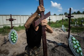 A funeral worker installs a cross with a number plate on the grave of an unidentified civilian killed by Russian troops during the Russian occupation in Bucha near Kyiv, Ukraine [File: Evgeniy Maloletka/AP Photo]