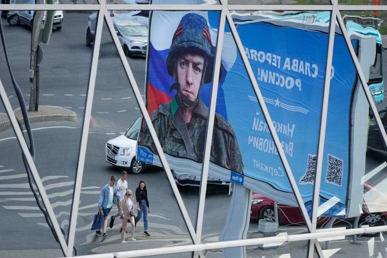 A billboard with a portrait of a Russian soldier and the words "Glory to the heroes of Russia" is reflected in a shopping mall in St. Petersburg