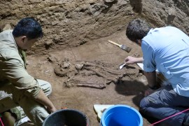 Two archaeologists working alongside each other to uncover a skeleton discovered in the mud of an Indonesian cave