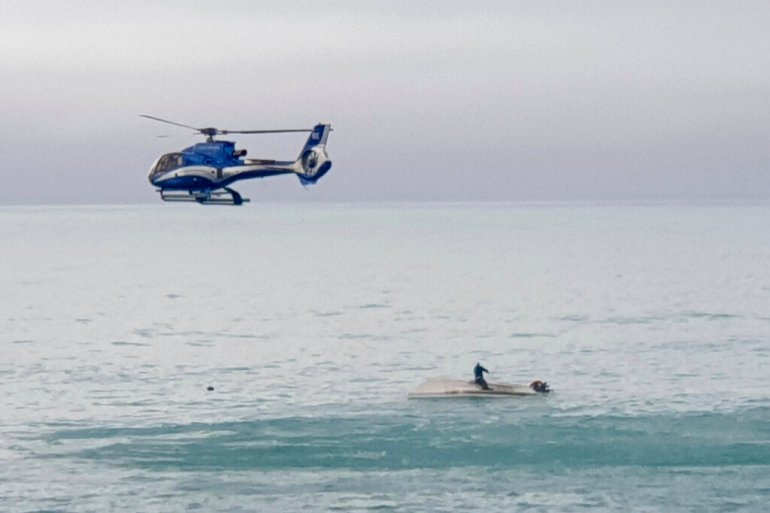 2022년 9월 10일 토요일 뉴질랜드 카이코우라 해안에서 선체에 생존자가 앉아 있는 뒤집힌 보트 위로 헬리콥터가 날아가고 있다. [AP]