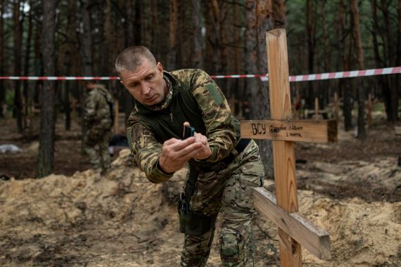 Oleg Kotenko, the commissioner for issues of missing people under special circumstances, uses his smartphone to film the grave of a Ukrainian soldier in Izyum, Ukraine