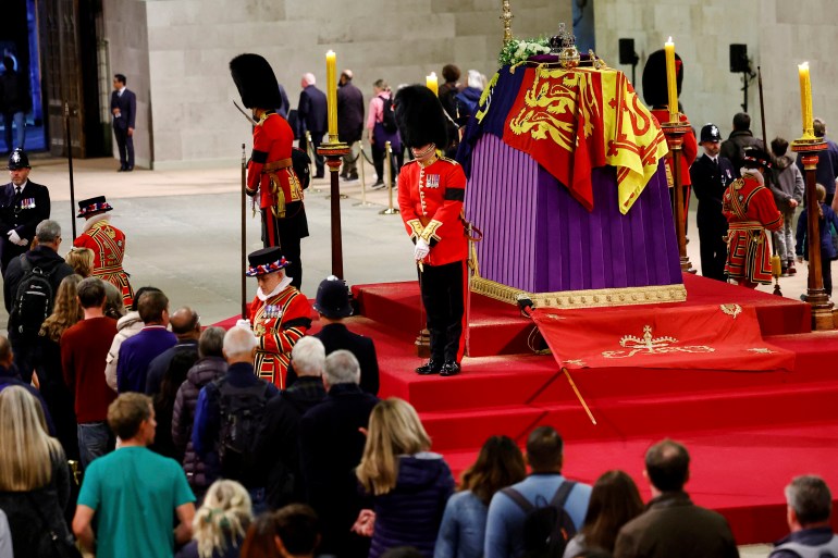 Members of the public walking past the queen's coffin with soldiers in ceremonial dress and bearskin hats standing guard
