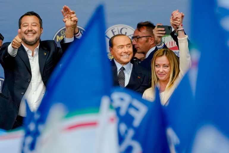 The League's Matteo Salvini, Forza Italia's Silvio Berlusconi, and Brothers of Italy's Giorgia Meloni smile and wave amid flags at their final campaign rally