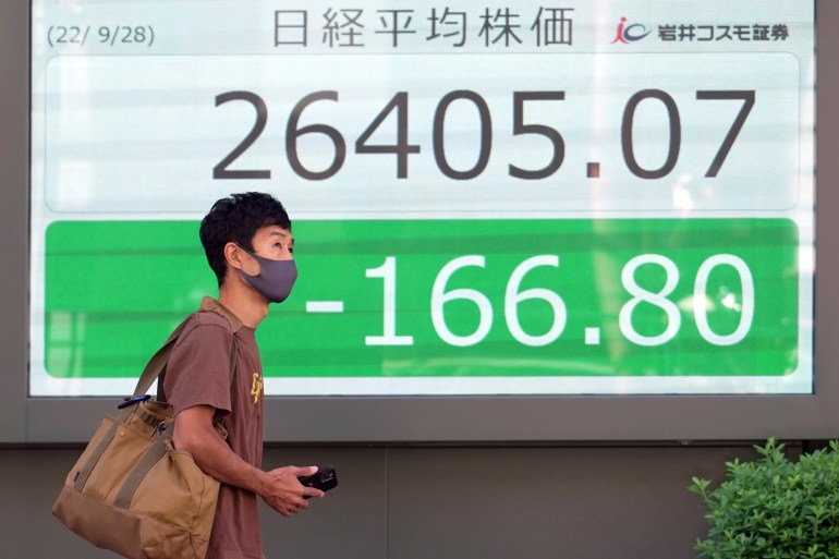 A person wearing a protective mask walks in front of an electronic stock board showing Japan's Nikkei 225 index at a securities firm Wednesday in Tokyo.