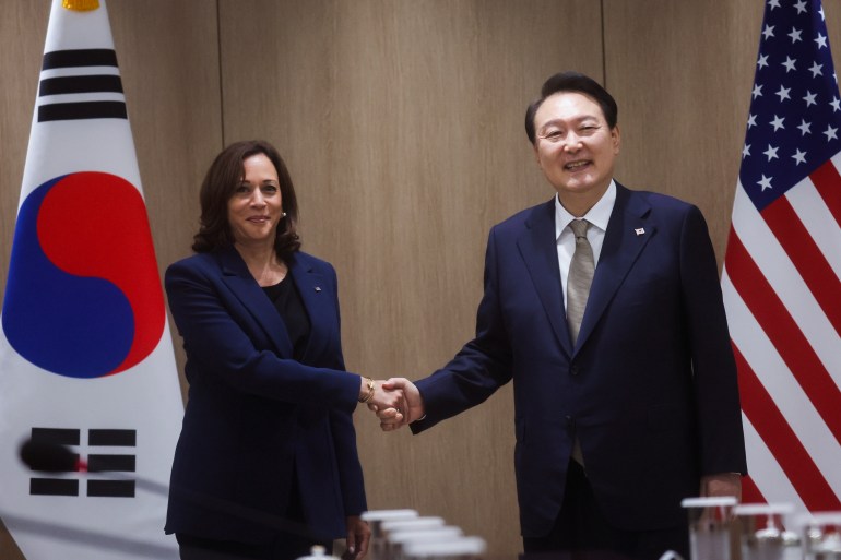 Kamala Harris, in front of a South Korean flag, shakes hands with a smiling Yoon Suk-yeol