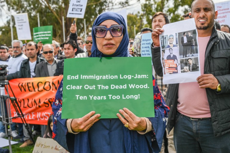 A woman in a blue headscarf and robe stands in front of the crowd of more than a thousand protesters, holding a placard that calls for an end to her 10 years of temporary visas. It reads: 'End Immigration Log-Jam: Clear out the Dead Wood. Ten Years too Long!