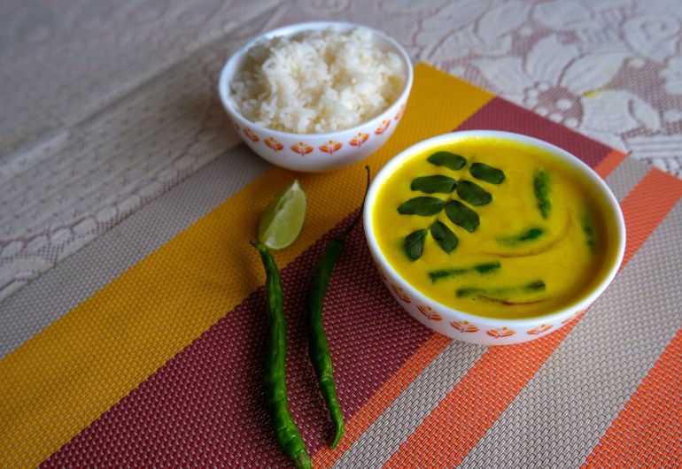 A bowl of rice sits next to a bowl of diya bath toppings