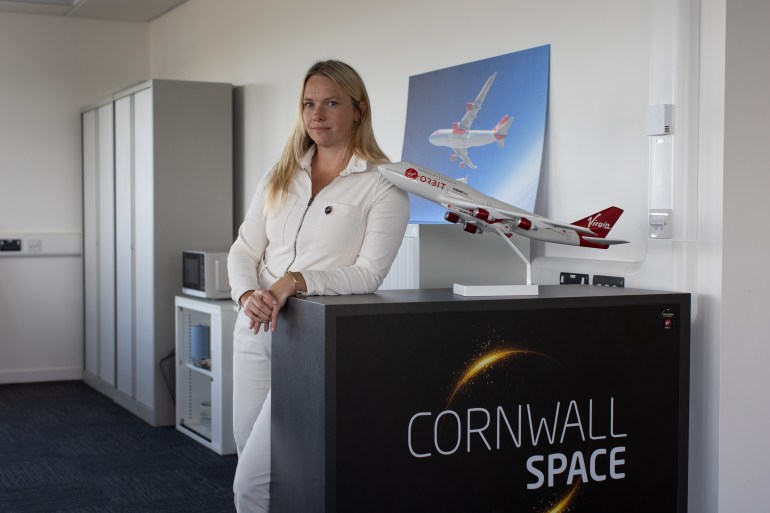 A photo of Mel Thorpe standing in front of a stand with the words "Cornell space" on the front and a model of an aeroplane on top.