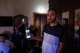 A man shows a picture on his phone in a dark room, others are in the background