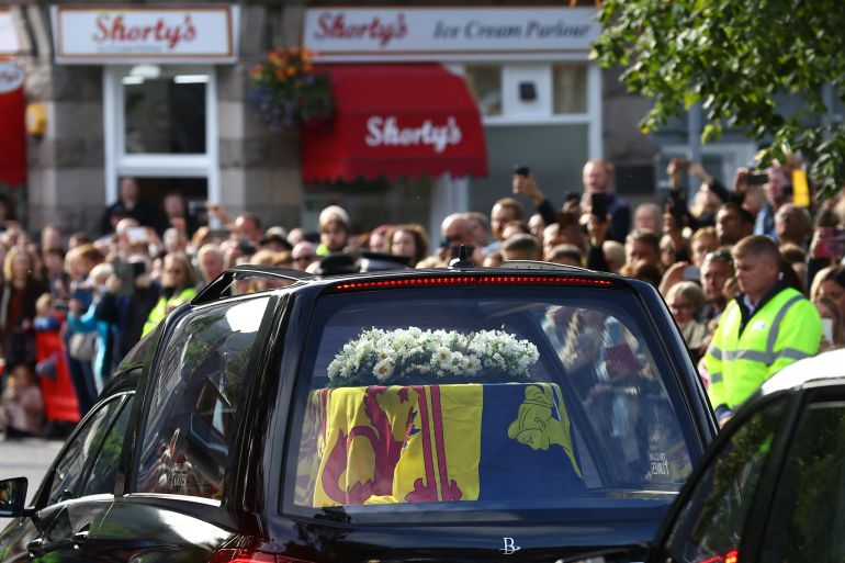 People line the street as a hearse carrying the coffin of Queen Elizabeth II passes through the village of Ballater in Scotland