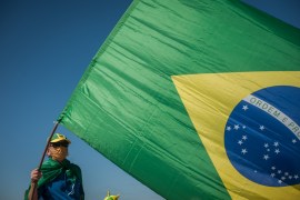 A Man is seen and holding a flag of Brazil .
