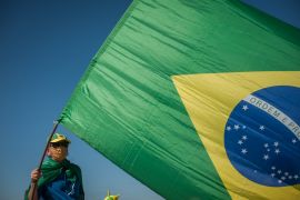 A Man is seen and holding a flag of Brazil .