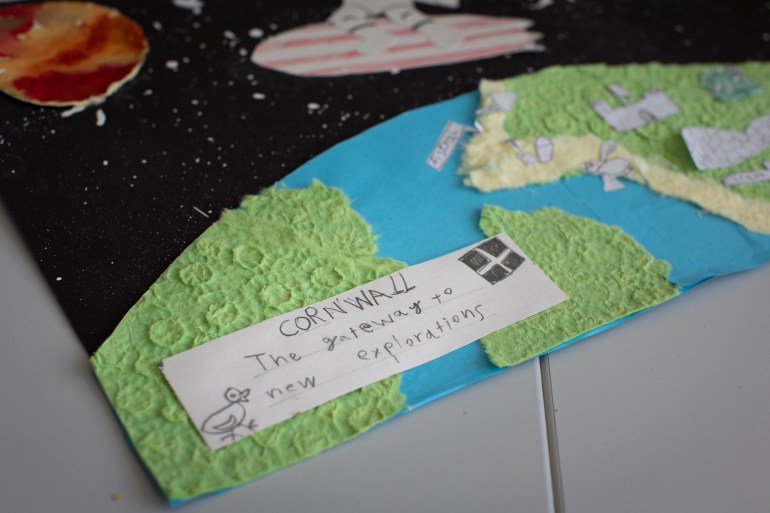 A photo of a poster of space with the earth peeking in the corner of the poster and a piece of paper stuck on it with the words "Cornwall: The gateway to new exploring."