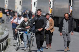Russian men, some pushing their bicycles, walk along a road after passing through customs at the Georgia-Russia border checkpoint of Verkhnii Lars, Georgia. [Zurab Kurtsikidze/EPA]