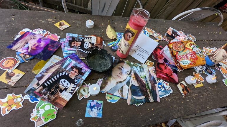 A photo of a table made from three planks of wood with stickers, photos and a prayer candle on top of them.
