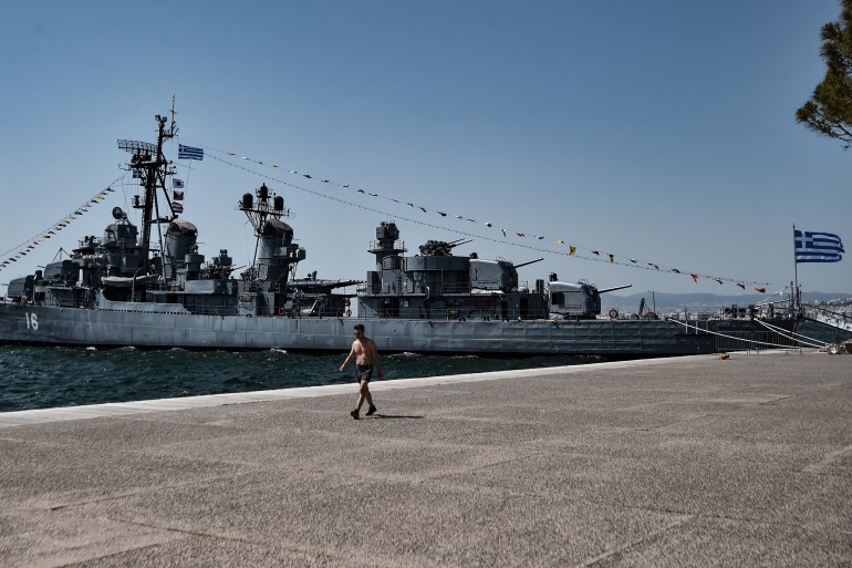 A man walks next to a war ship museum on the waterfront of Thessaloniki