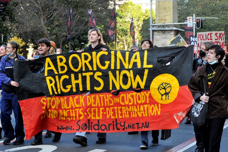 Protesters walk with a banner in the colours of the Aboriginal flag reading 'Aboriginal rights now'