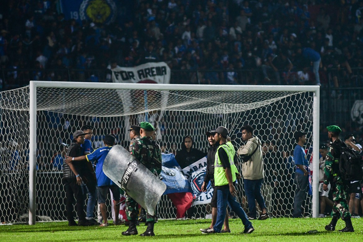 Police with riot shields on the pitch in Malang after the match between Arema FC and Persebaya Surabaya. They are carrying riot shields. Some are in high-viz jackets. The goal is behind them.