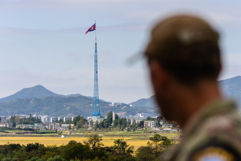 A soldier stands in the foreground with the truce village of Panmunjom and mountains behind him