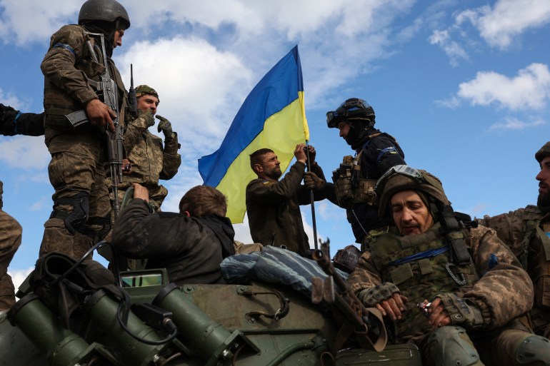 Ukrainian soldiers fly a blue and yellow Ukrainian flag as they travel on top of an armoured personnel carrier near Lyman