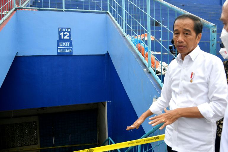Joko Widodo in white stands at gate which is cordoned off with yellow barricade tape
