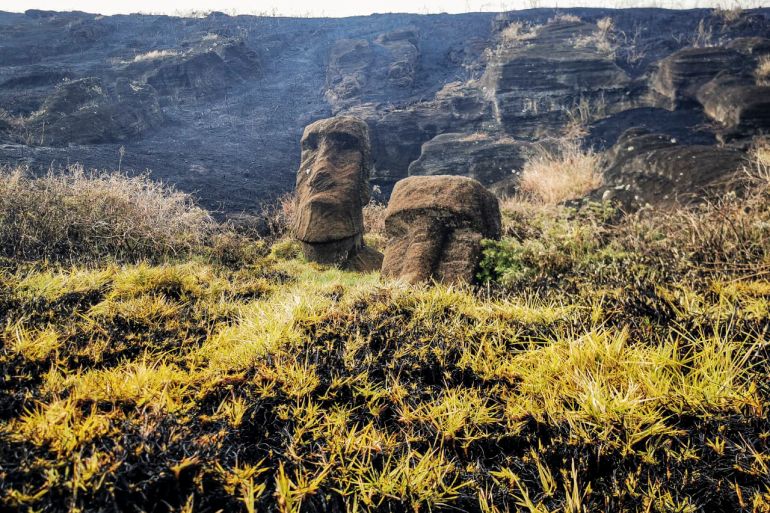 Moai stone statues are seen as smoke rises behind them.