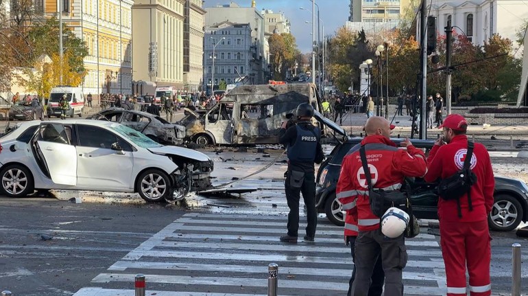 Two rescuer workers at the scene of a Russian cruise missile attack on a Kyiv street with destroyed cars and buildings behind