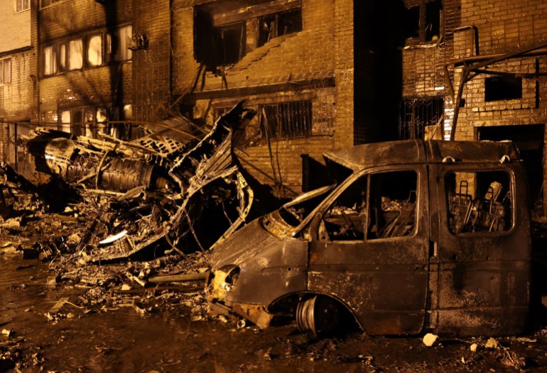 Burned out vehicles and some of the wreckage of the crashed Sukhoi fighter jet next to the damaged block of flats in the Russian city of Yeysk in a yellow glow