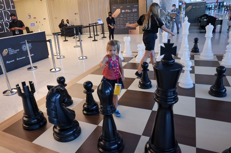A child reaches for a giant chess piece on a board