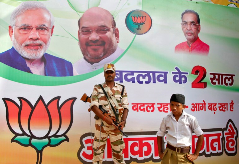 A policeman stands guard as a volunteer (bottom R) of the Hindu nationalist organisation Rashtriya Swayamsevak Sangh (RSS) looks on in front of a hoarding featuring Prime Minister Narendra Modi (L) and Amit Shah, president of India's ruling Bharatiya Janata Party (BJP), outside the venue of the party's national executive meeting in Allahabad