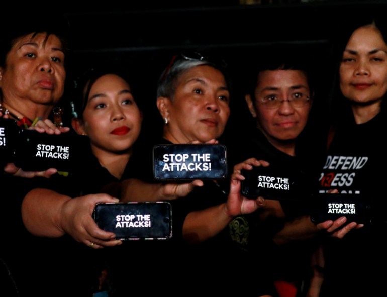 Journalists, including Rappler CEO Maria Ressa, raise their smart phones with words "STOP THE ATTACKS!" in a rally for press freedom in Quezon City, Philippines in 2019 [Eloisa Lopez/Reuters]