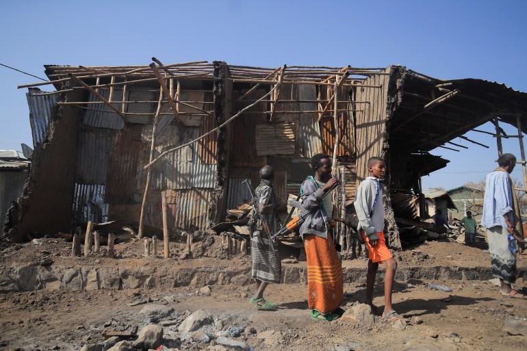 Residents and militias stand next to houses destroyed by an airstrike during the fight between the Ethiopian National Defence Forces (ENDF) and the Tigray People's Liberation Front (TPLF) forces in Kasagita town, Afar region, Ethiopia, February 25, 2022. Picture taken February 25, 2022.