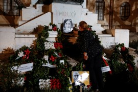 An activist places a portrait of assassinated anti-corruption journalist Daphne Caruana Galizia and a poster depicting former Prime Minister Joseph Muscat on the Great Siege Monument after an official wreath-laying ceremony, as people nearby protest against the authorities' lack of action over high-profile corruption cases first revealed by Caruana Galizia, in Valletta, Malta