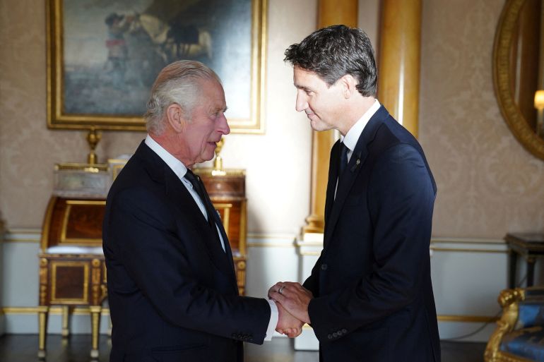 Profile of Trudeau and King Charles wearing black suits, Trudeau taller than the king smiling.