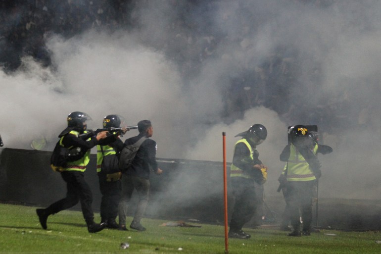 Indonesia police fire off clouds of tear gas as they stand on the pitch after Arema vs Persebaya at Kanjuruhan Stadium.