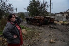A woman stands next to a destroyed armoured fighting vehicle in the liberated village of Kamianka, amid Russia's attack on Ukraine, in Kharkiv region
