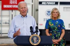 Joe Biden speaks at a lectern while First Lady Jill Biden watches from behind him.