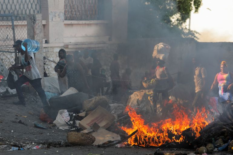 People walk past a burning street barricade during a protest against the government and rising fuel prices