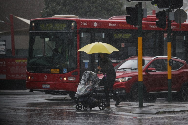A woman with a baby buggy and an umbrella tries to cross a rainy road in Sydney