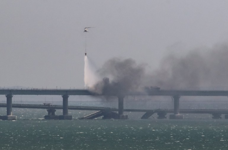 A helicopter drops water to extinguish burnt fuel tanks next to damaged sections of the Kerch bridge.