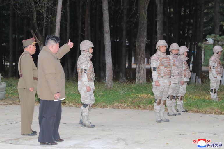 Kim Jong Un gives a thumbs up to soldiers in fatigues standing near trees.