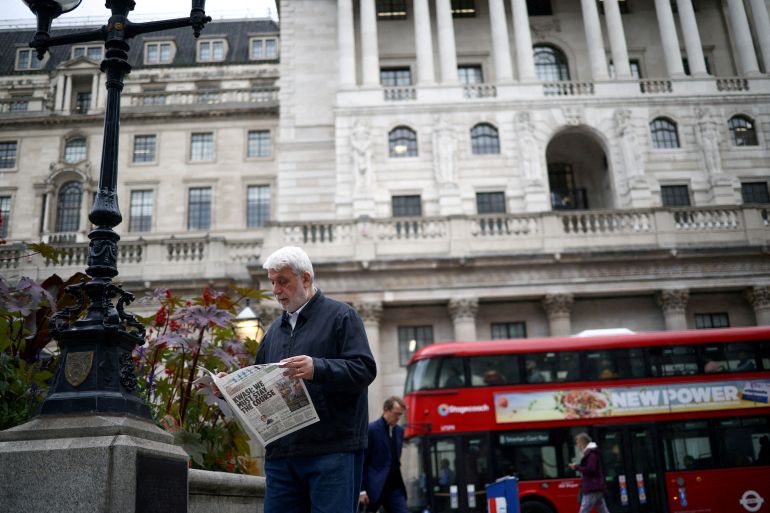 A person reads a newspaper outside the Bank of England in the City of London financial district