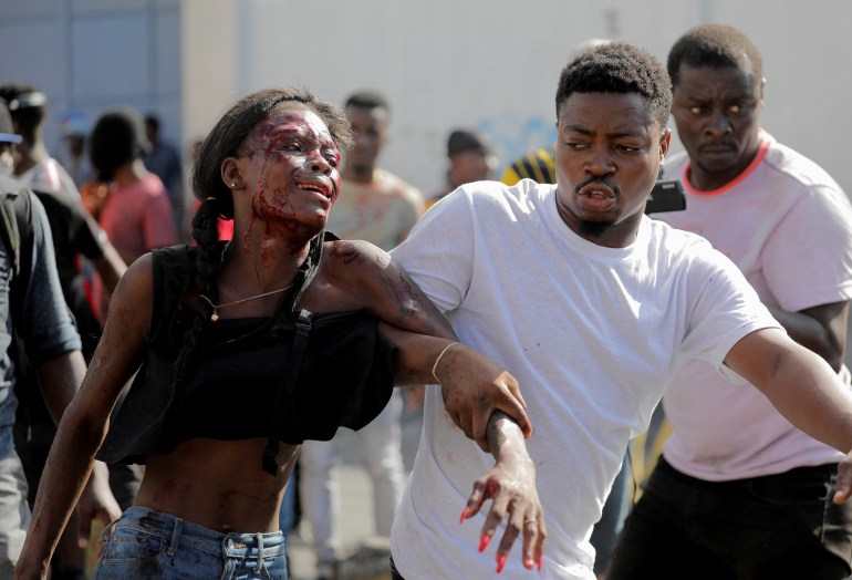A man helps a woman with blood on her face after security guards saw her looting in a hotel during a protest demanding the resignation of Haiti's Prime Minister Ariel Henry after weeks of shortages, in Port-au-Prince, Haiti October 10, 2022. REUTERS/Ralph Tedy Erol