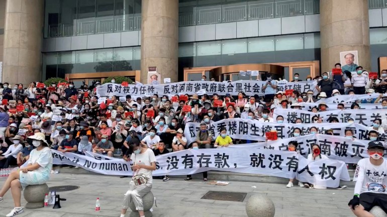 Protesters hold banners demanding their deposits be returned outside outside a People's Bank of China building in Zhengzhou