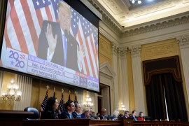 A January 6 Capitol riot hearing is held with a video of former US President Donald Trump playing on a large screen above committee members.